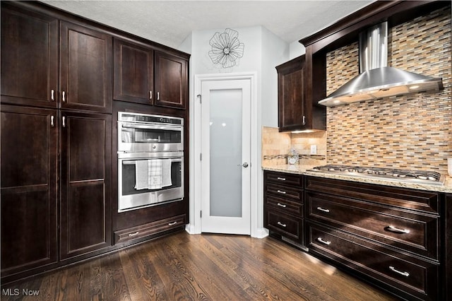 kitchen featuring appliances with stainless steel finishes, light stone countertops, wall chimney range hood, and dark wood-style floors