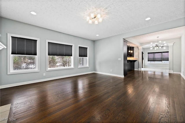 unfurnished living room with a wealth of natural light, baseboards, dark wood-type flooring, and a notable chandelier