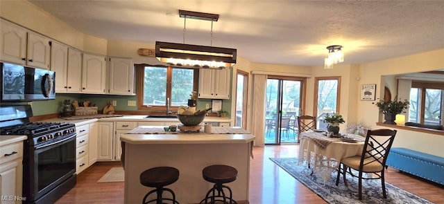 kitchen with white cabinetry, stainless steel microwave, a kitchen island, and black range with gas stovetop