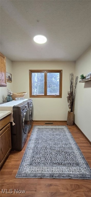 clothes washing area featuring light wood-type flooring, cabinet space, baseboards, and washing machine and clothes dryer