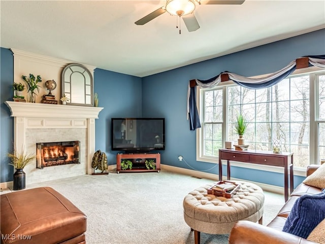 carpeted living area with baseboards, a ceiling fan, and a high end fireplace