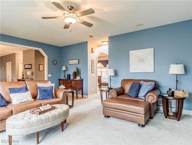 living room featuring ceiling fan, arched walkways, baseboards, and light colored carpet