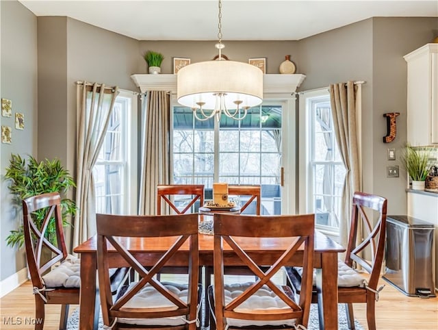 dining space featuring light wood-style floors, a notable chandelier, and baseboards