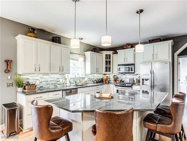 kitchen with stainless steel appliances, decorative backsplash, white cabinets, a sink, and a kitchen breakfast bar