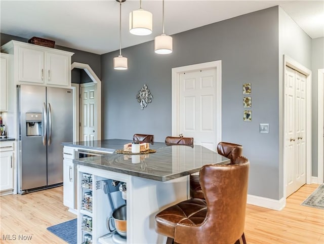 kitchen featuring light wood-type flooring, stainless steel refrigerator with ice dispenser, a kitchen island, and white cabinetry