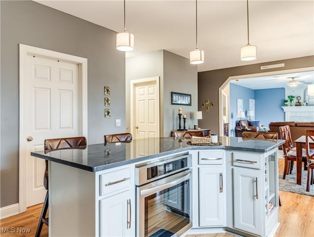 kitchen with hanging light fixtures, light wood-style floors, white cabinetry, and stainless steel oven