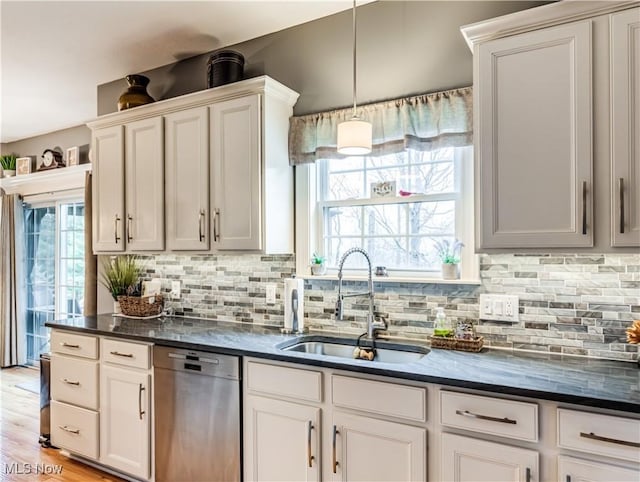 kitchen with decorative light fixtures, backsplash, stainless steel dishwasher, light wood-style floors, and a sink