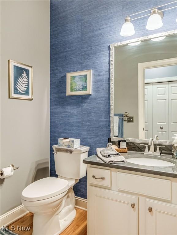 half bathroom featuring wood finished floors, toilet, and baseboards