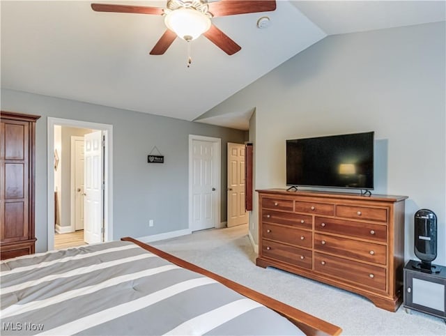 bedroom featuring light colored carpet, ensuite bathroom, a ceiling fan, vaulted ceiling, and baseboards