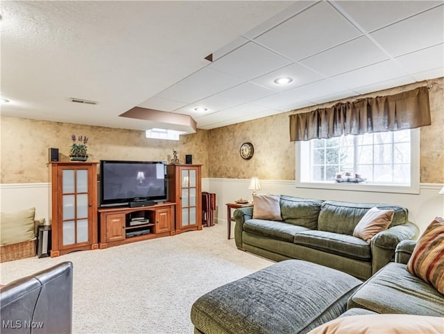 carpeted living room with a wainscoted wall, a drop ceiling, visible vents, and wallpapered walls