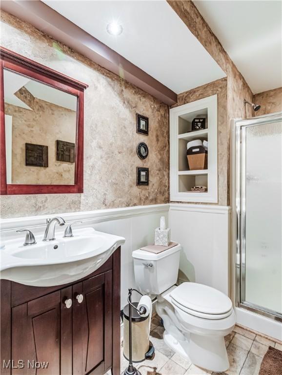 full bathroom with built in shelves, a wainscoted wall, a shower stall, and toilet