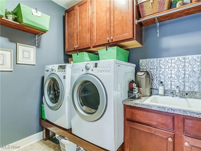 laundry area with light tile patterned floors, a sink, baseboards, independent washer and dryer, and cabinet space