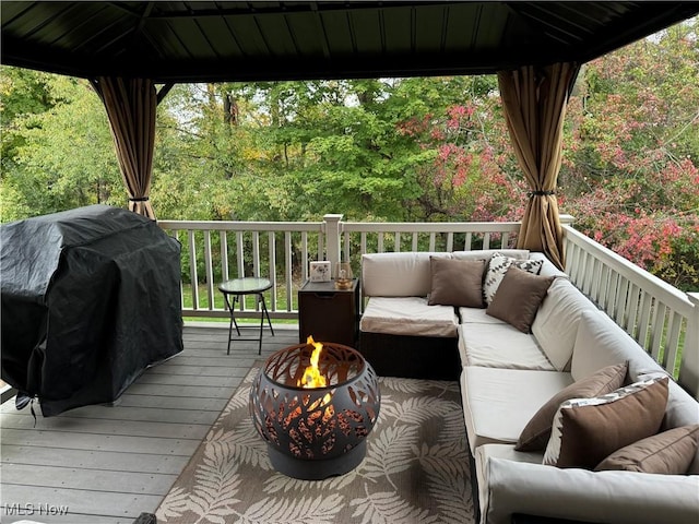 deck with an outdoor living space with a fire pit, a grill, a wooded view, and a gazebo