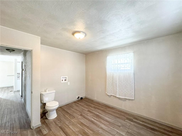 bathroom with a textured ceiling, wood finished floors, toilet, and baseboards