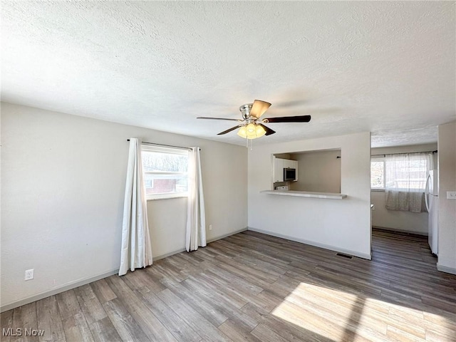 empty room featuring a wealth of natural light, visible vents, and wood finished floors