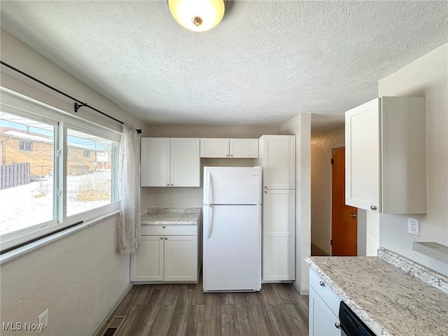 kitchen featuring dark wood-style floors, visible vents, freestanding refrigerator, white cabinets, and a textured ceiling