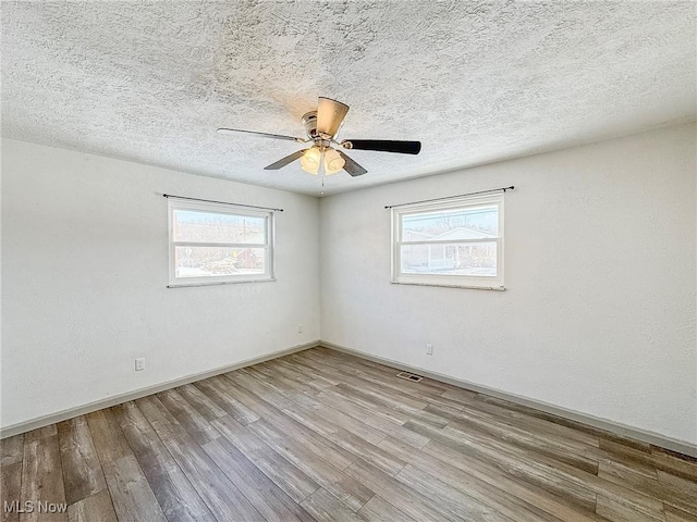 unfurnished room with a textured ceiling, wood finished floors, visible vents, and baseboards