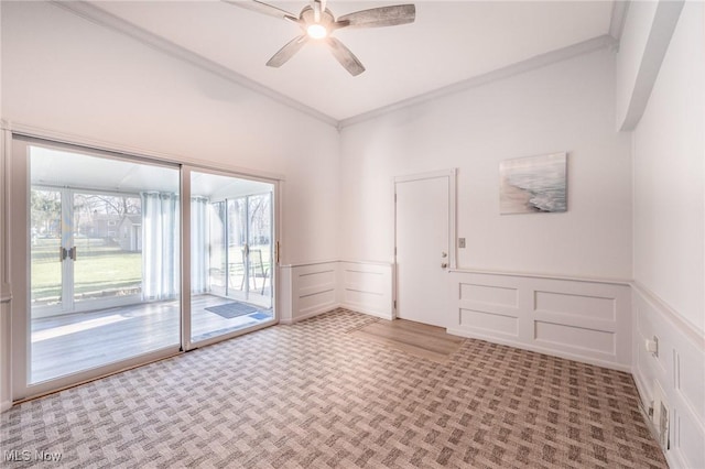 carpeted empty room with wainscoting, crown molding, a decorative wall, and ceiling fan