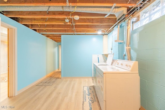 clothes washing area with concrete block wall, light wood-style flooring, washing machine and dryer, laundry area, and baseboards