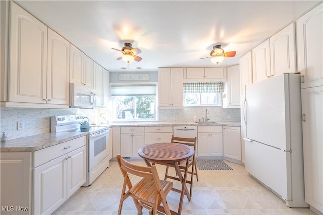 kitchen featuring white appliances, white cabinets, a ceiling fan, a sink, and backsplash