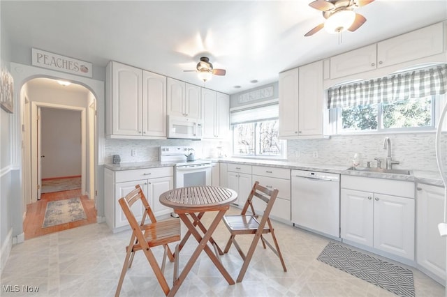 kitchen with arched walkways, ceiling fan, white appliances, and a sink