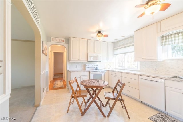 kitchen with arched walkways, ceiling fan, white appliances, white cabinetry, and decorative backsplash