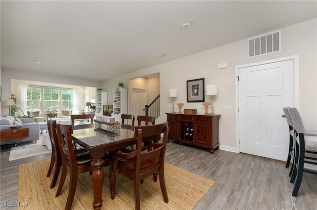 dining space featuring visible vents, light wood-style flooring, baseboards, and stairs