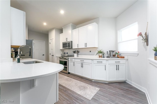 kitchen with stainless steel appliances, light countertops, light wood-style floors, white cabinets, and a sink