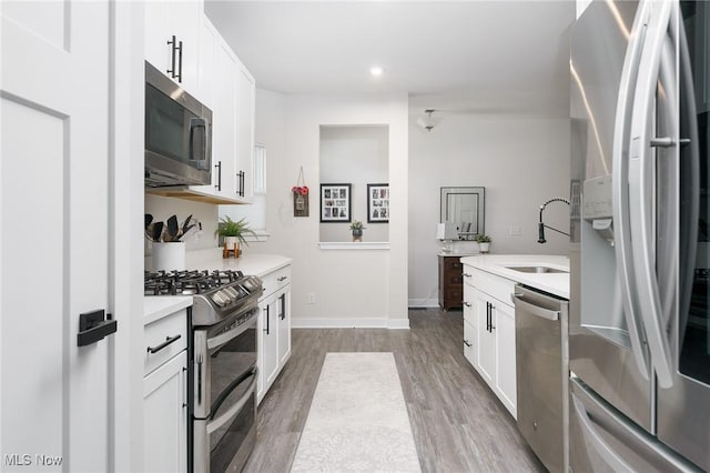 kitchen with stainless steel appliances, wood finished floors, a sink, and light countertops