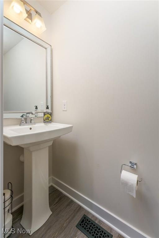 half bathroom with visible vents, baseboards, toilet, wood finished floors, and a sink