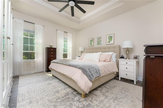 bedroom featuring ceiling fan, wood finished floors, a raised ceiling, and baseboards