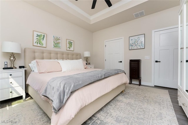 bedroom with a tray ceiling, visible vents, ceiling fan, wood finished floors, and baseboards