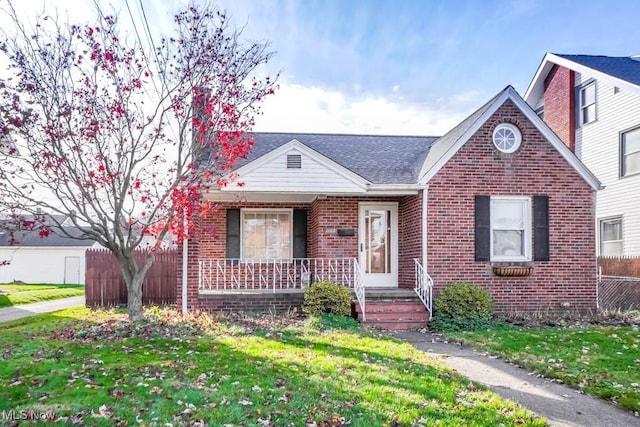 view of front of property with brick siding, roof with shingles, fence, a porch, and a front yard