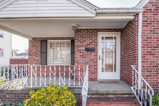 doorway to property featuring fence and brick siding