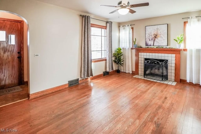 unfurnished living room with arched walkways, a fireplace, visible vents, a ceiling fan, and wood finished floors