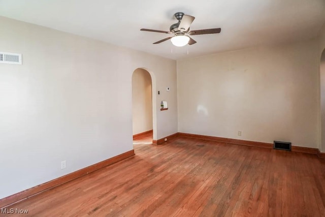 spare room featuring light wood-type flooring, baseboards, visible vents, and arched walkways