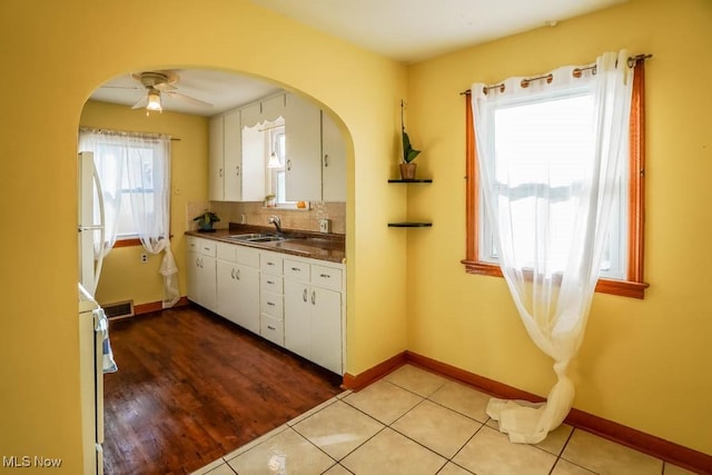 kitchen featuring decorative backsplash, white cabinets, dark countertops, freestanding refrigerator, and a sink