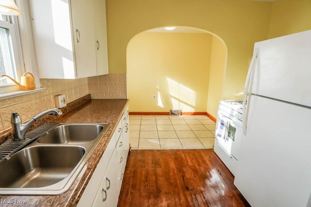 kitchen with white appliances, tasteful backsplash, white cabinets, dark countertops, and a sink