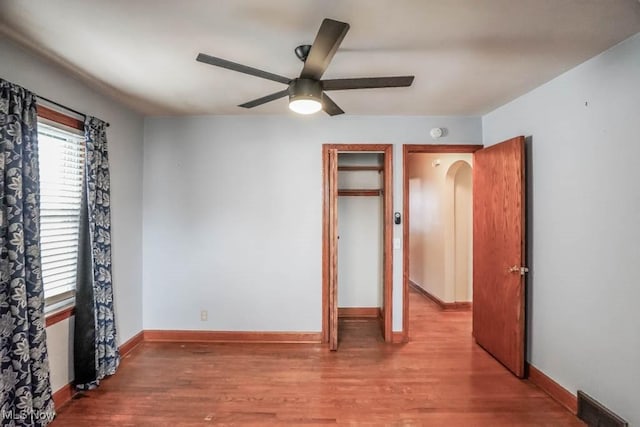 unfurnished bedroom featuring arched walkways, wood finished floors, visible vents, and baseboards