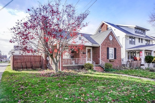 view of front of property featuring brick siding, a front lawn, a porch, and fence