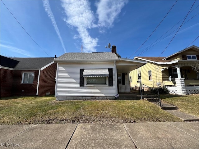 back of property featuring roof with shingles, a chimney, a porch, and a yard