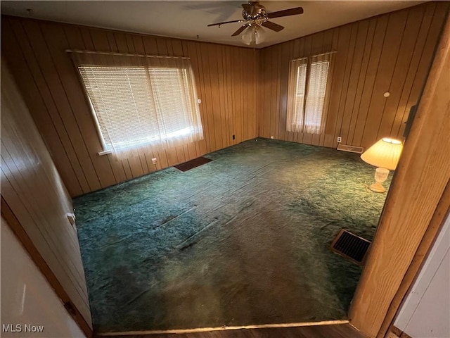 unfurnished room with wooden walls, carpet flooring, visible vents, and a ceiling fan