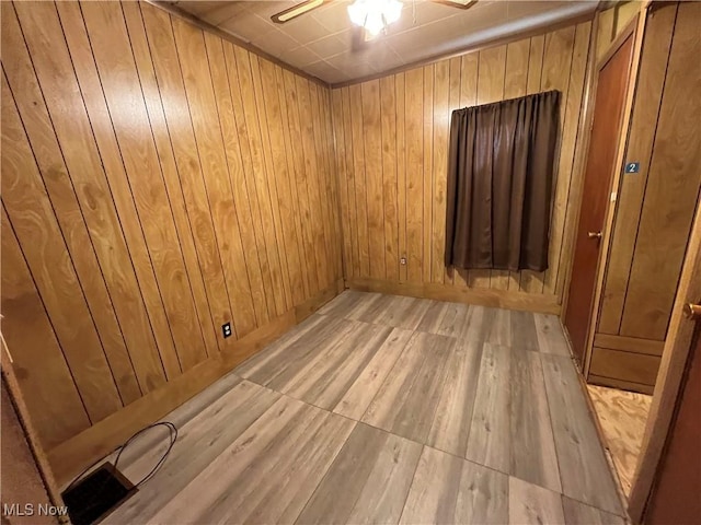 unfurnished room featuring a ceiling fan, wooden walls, and light wood finished floors