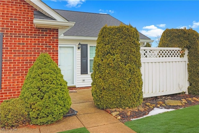 view of side of property featuring brick siding, roof with shingles, and fence