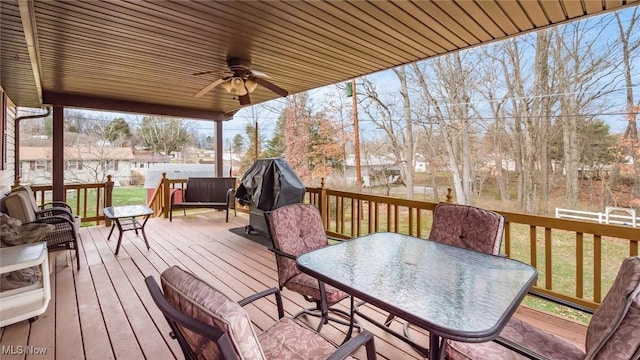 deck featuring ceiling fan, outdoor dining area, and a lawn