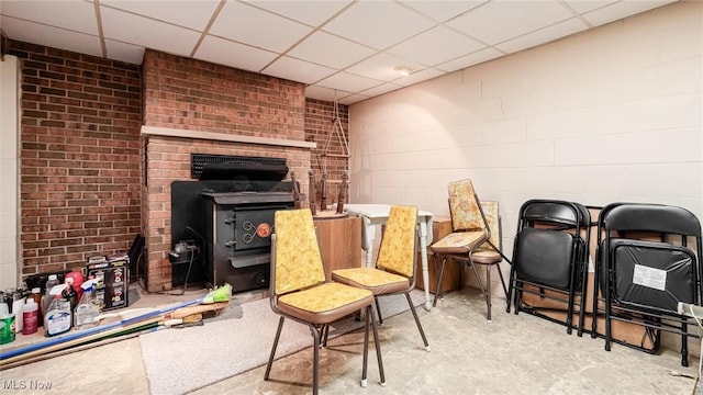 living area featuring a paneled ceiling, a wood stove, brick wall, and concrete block wall