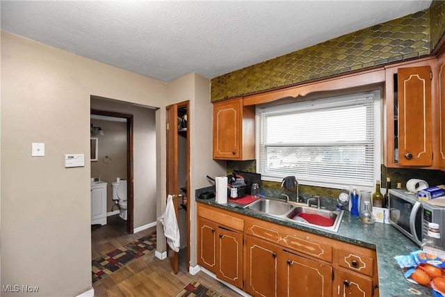 kitchen featuring dark wood-style flooring, a sink, stainless steel microwave, dark countertops, and washing machine and clothes dryer