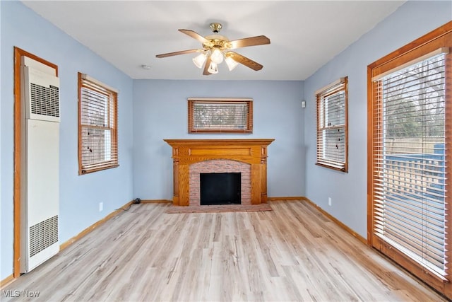 unfurnished living room with a fireplace, light wood-style floors, a heating unit, ceiling fan, and baseboards