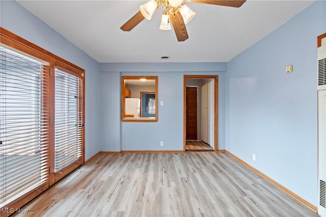 spare room featuring a ceiling fan, visible vents, baseboards, and wood finished floors