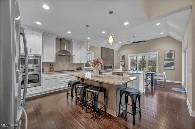 kitchen featuring stainless steel appliances, wall chimney range hood, a peninsula, and a wealth of natural light